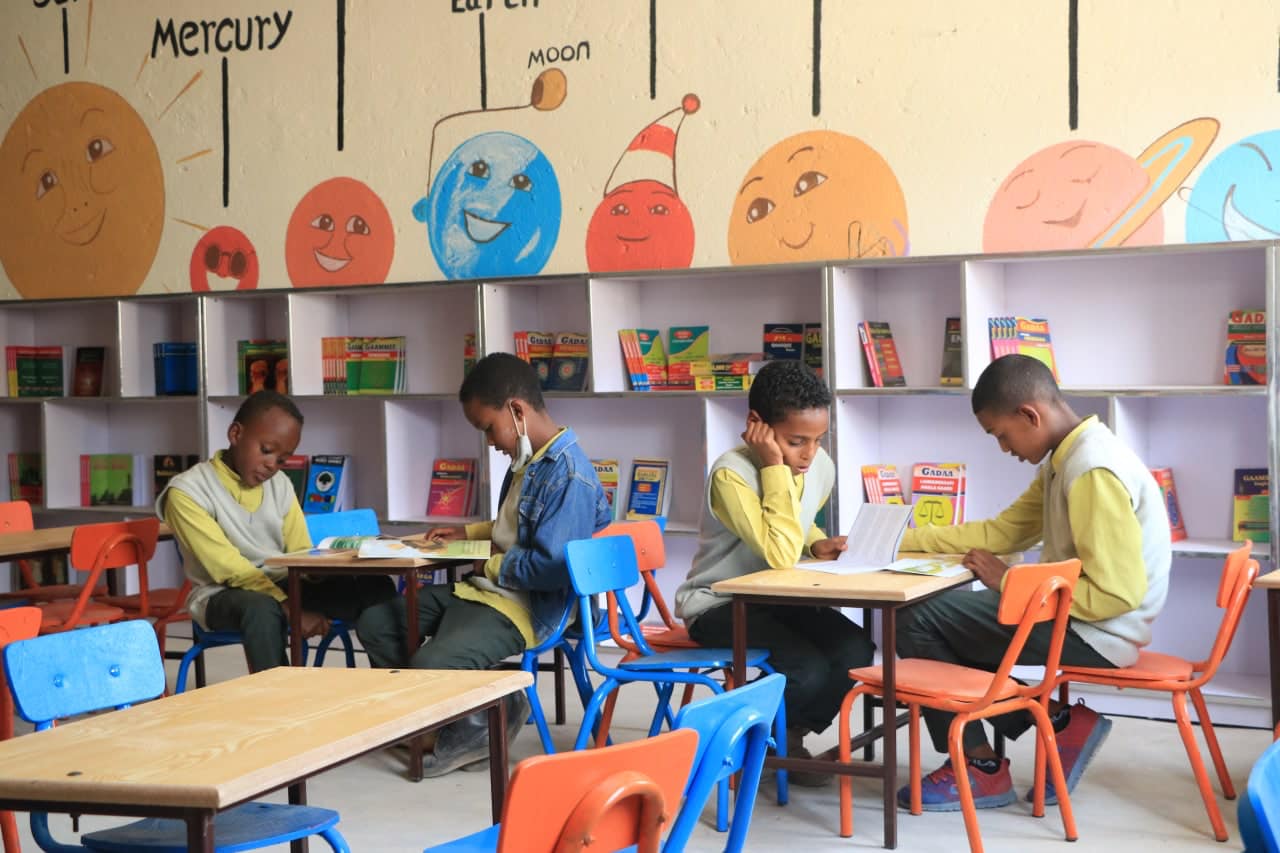 Students reading at tables in the Burka Wayo library, painted planets on the wall above