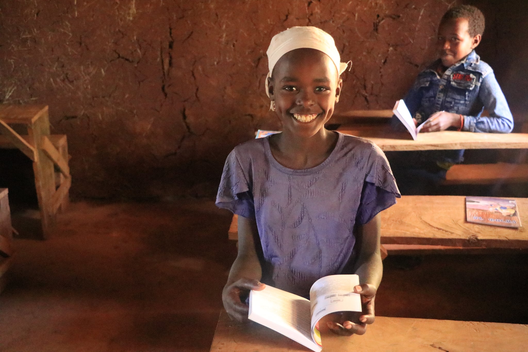 A smiling girl holds an open book at her desk in the Daro school library